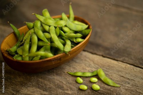 edamame beans in wooden bowl on textured wooden table.