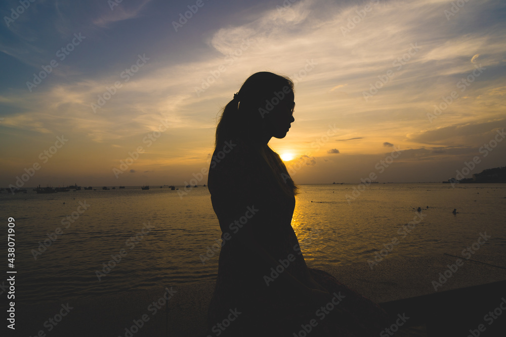 Back view silhouette young girl asian with depressed pose on the beach at sunset. Beautiful blonde woman with long hair depressing at the ocean. Concept of depress, sad