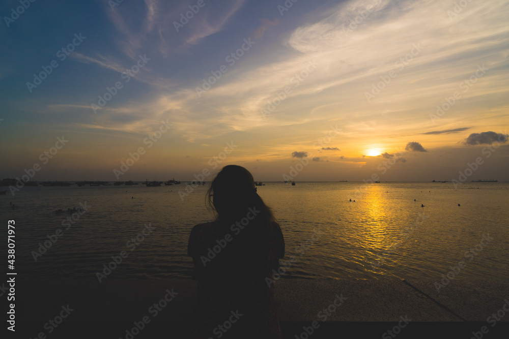 Back view silhouette young girl asian with depressed pose on the beach at sunset. Beautiful blonde woman with long hair depressing at the ocean. Concept of depress, sad