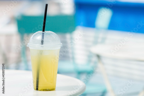 On the table in a cozy cafe is a lemonade, a plastic glass. Cooling drink with lemon and mint. Light blue-white background.