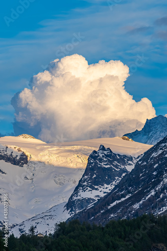 Alpine mountain landscape above Val Herens in Switzerland at sunset with peaks covered by snow and a very big cloud
