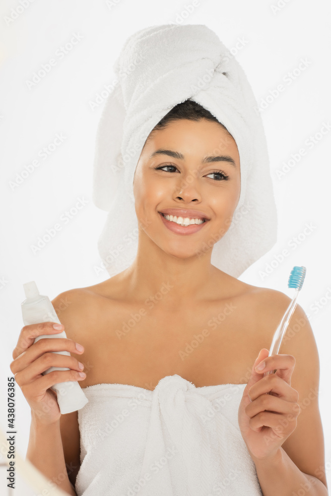 positive young african american woman wrapped in towels holding toothbrush and toothpaste in bathroom positive young african american woman wrapped in towels holding toothbrush and toothpaste in bathroom