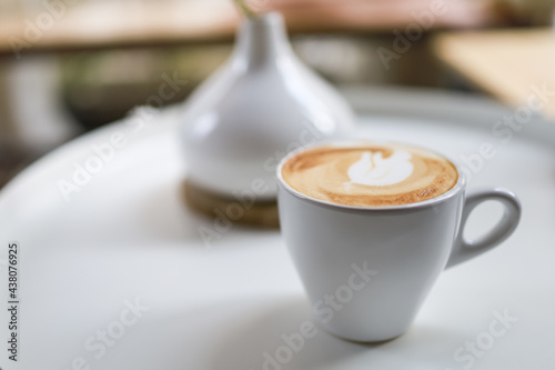 Closeup of white cup of hot coffee latte with milk foam on white round table.