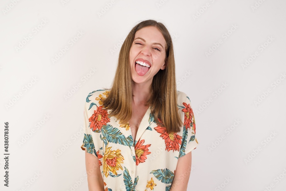 Beautiful caucasian woman with happy and funny face smiling and showing tongue. Wearing casual clothes and standing against white studio background. Beautiful caucasian woman with happy and funny face smiling and showing tongue. Wearing casual clothes and standing against white studio background.