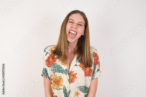 Beautiful caucasian woman with happy and funny face smiling and showing tongue. Wearing casual clothes and standing against white studio background. © Jihan