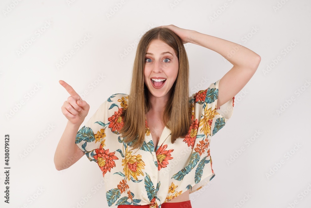 Portrait of young woman with shocked facial expression, showing something amazing on blank space, one hand on her head and pointing with forefinger. OMG concept. Portrait of young woman with shocked facial expression, showing something amazing on blank space, one hand on her head and pointing with forefinger. OMG concept.