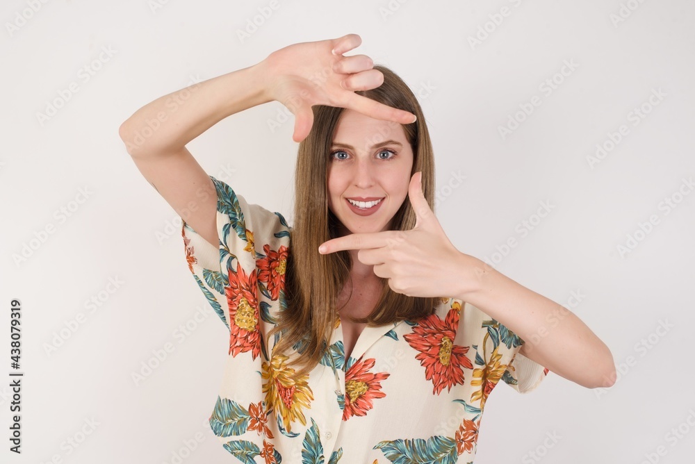 Portrait of young blonde positive female with cheerful expression, dressed in casual light blue sweater, has good mood, gestures finger frame actively at camera. Portrait of young blonde positive female with cheerful expression, dressed in casual light blue sweater, has good mood, gestures finger frame actively at camera.