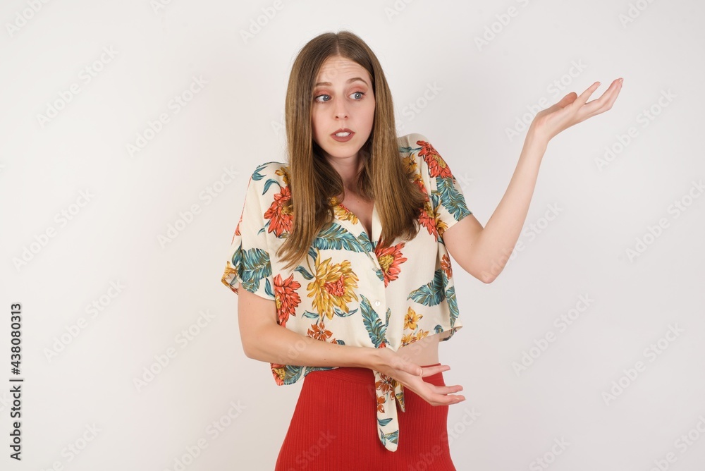 Beautiful European girl pointing aside with both hands showing something strange and saying: I don't know what is this. Standing against gray background. Advertisement concept. Beautiful European girl pointing aside with both hands showing something strange and saying: I don't know what is this. Standing against gray background. Advertisement concept.