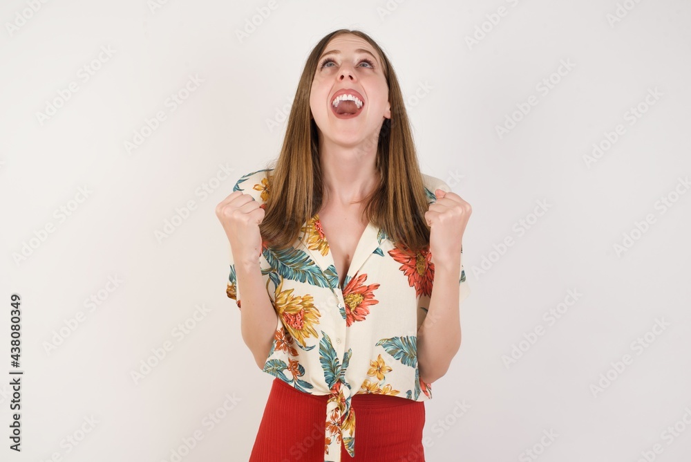 Portrait of beautiful blonde female looks with excitement up, keeps hands raised, notices something unexpected, poses indoors. Lovely woman reacts on sudden news. Portrait of beautiful blonde female looks with excitement up, keeps hands raised, notices something unexpected, poses indoors. Lovely woman reacts on sudden news.