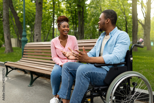 Happy handicapped black guy in wheelchair talking to his girlfriend at park, copy space