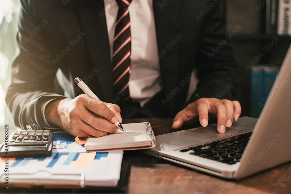 Businessman sitting at a table at home working on a laptop and writing down ideas in a notebook. Businessman sitting at a table at home working on a laptop and writing down ideas in a notebook.