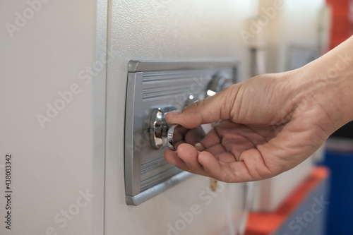 Close up of a hand unlocking a safe deposit box by turning a knob with numbers. Composite image between a hand photography 