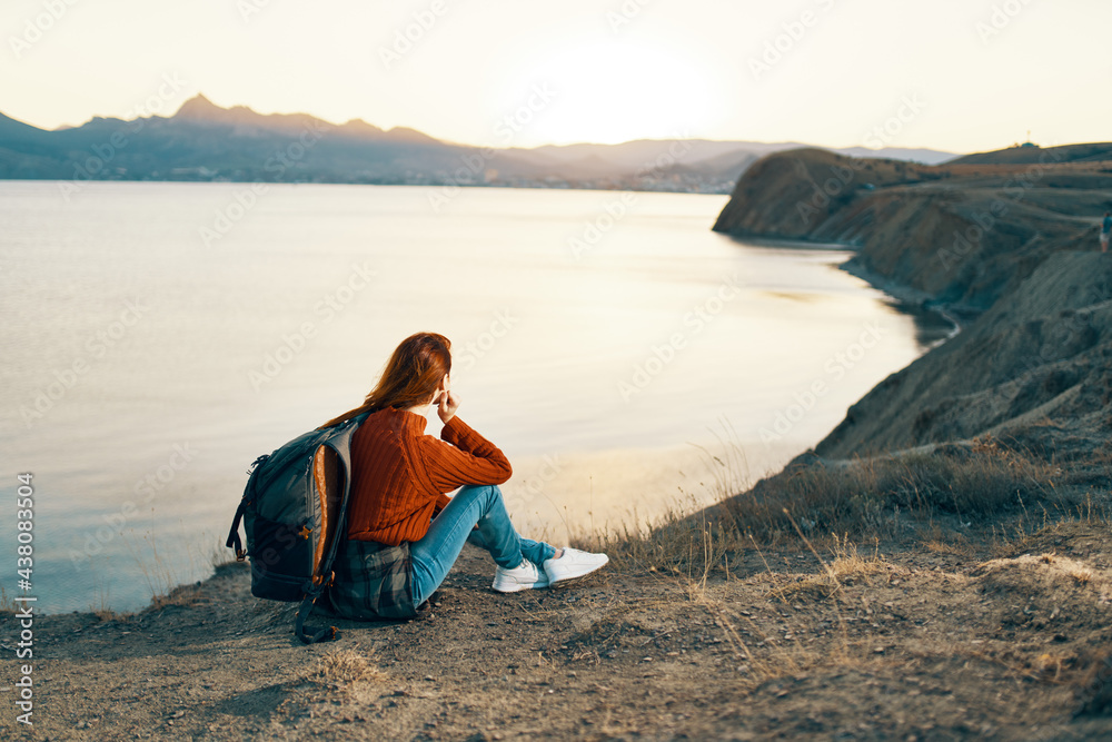 woman hiker with backpack in the mountains at sunset near the sea
