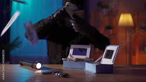 Funny robber in a balaclava finds jewelry on the table and tries them on himself