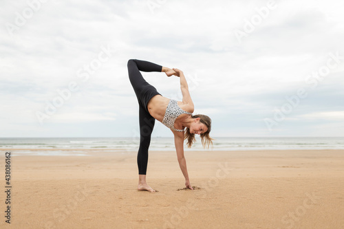 Blonde woman making yoga. She is in beach during cloudy sunset or sunrise. She is alone. She is wearing sportswear. She is caucasian girl from Germany