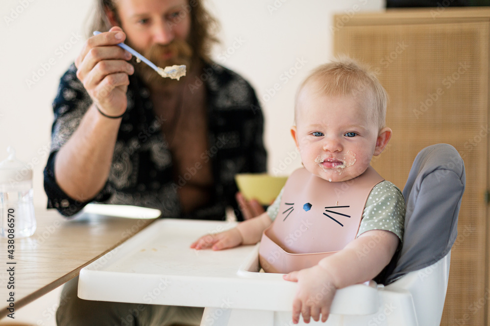 Man feeding baby son sitting in high chair Man feeding baby son sitting in high chair