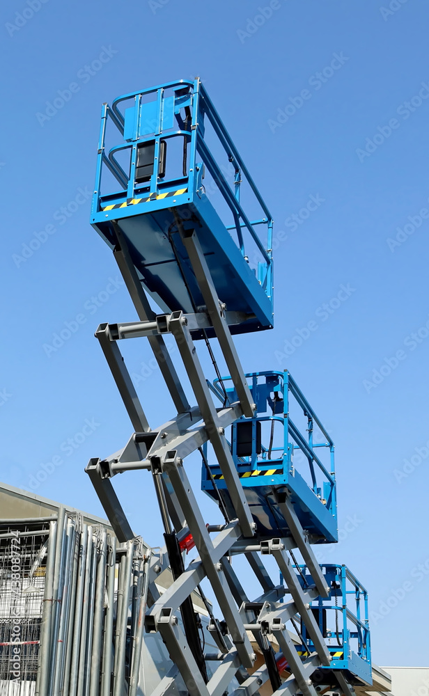 Fototapeta premium Three working platforms, called scissor elevator, against blue sky