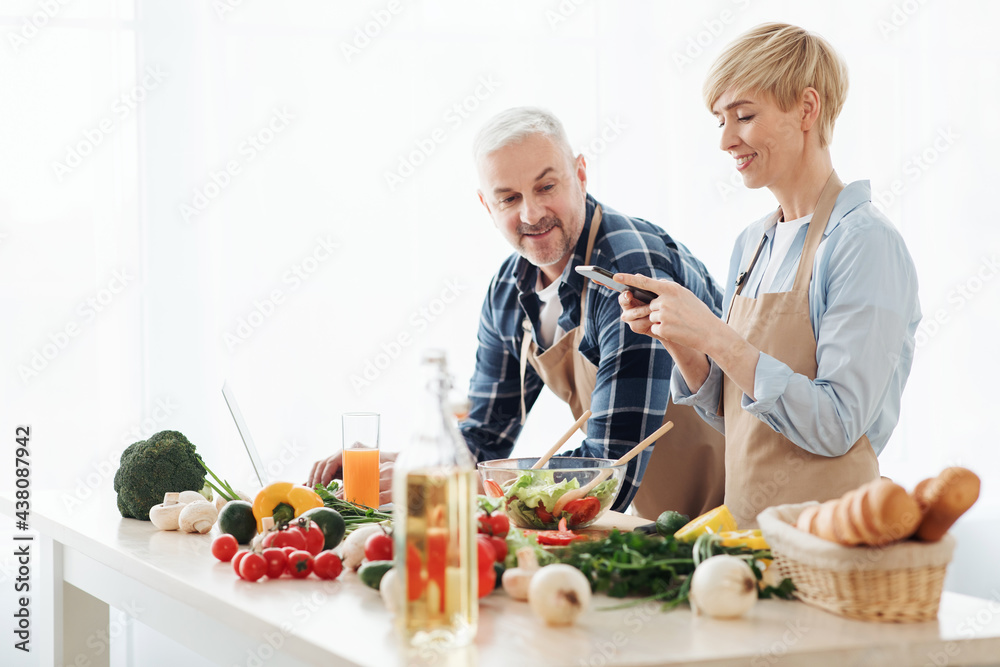 Senior couple recording video about vegetarian food on camera in kitchen