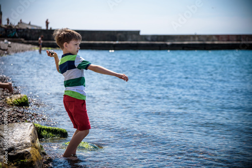 The little boy by the sea throws stones in water. Relaxation and vacation with kids. Happy childhood © pahis