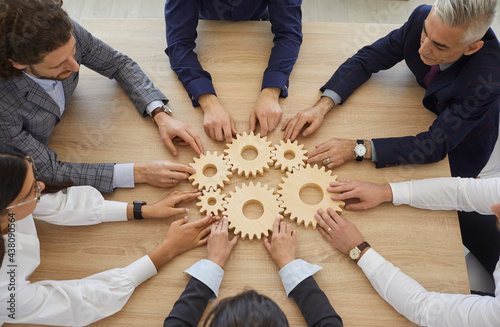 Team of entrepreneurs collaborate and develop effective business system. Group of senior and young business people join gearwheels as metaphor for good cooperation and teamwork, high angle, from above photo