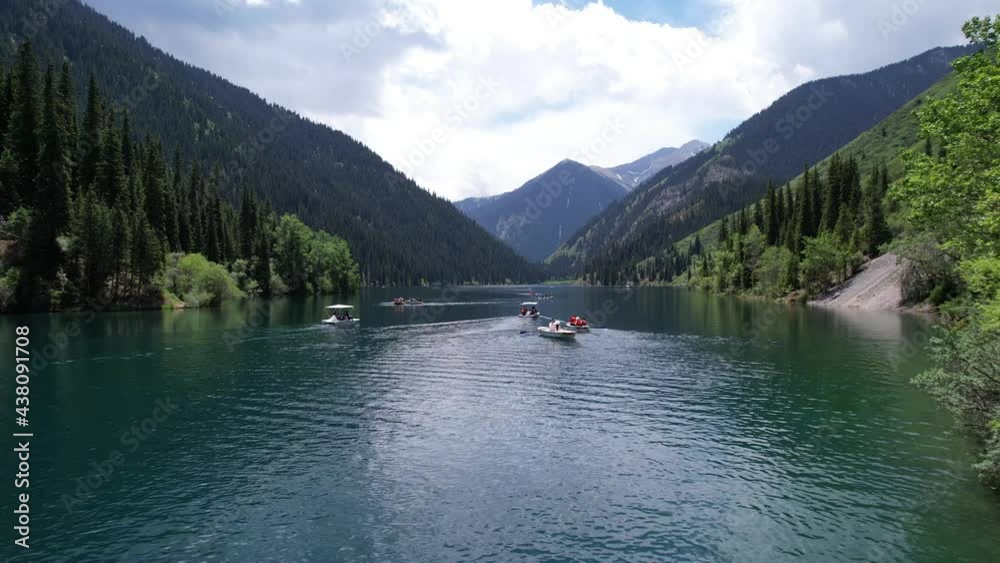 Kolsai mountain lake and green forest. Top view. People swim in boats and catamarans. They rest on the green meadows. The sun's rays shine on water. Clear water and tall coniferous trees. Kazakhstan Kolsai mountain lake and green forest. Top view. People swim in boats and catamarans. They rest on the green meadows. The sun's rays shine on water. Clear water and tall coniferous trees. Kazakhstan