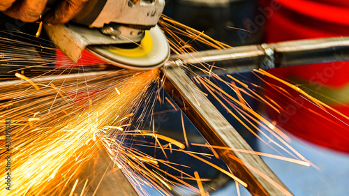 grinder sanding the metal, the steel rods, after having welded the pieces together, many golden sparks come out of the area where the disc is filing the metal