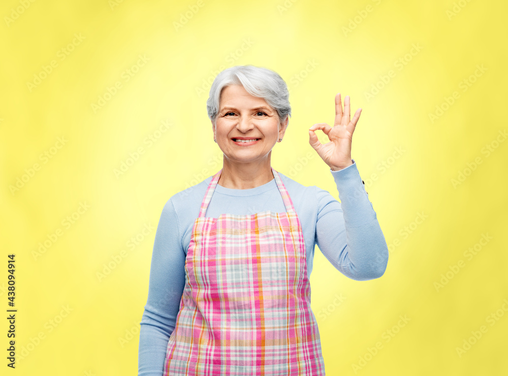 cooking, culinary and old people concept - portrait of smiling senior woman in kitchen apron showing ok hand sign over illuminating yellow background cooking, culinary and old people concept - portrait of smiling senior woman in kitchen apron showing ok hand sign over illuminating yellow background