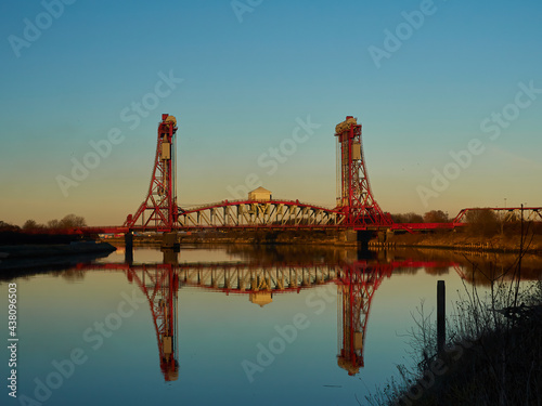 The Newport Bridge against a gradated blue and orange sky. The foreground shows the still, glassy River Tees reflecting the scene and sky.