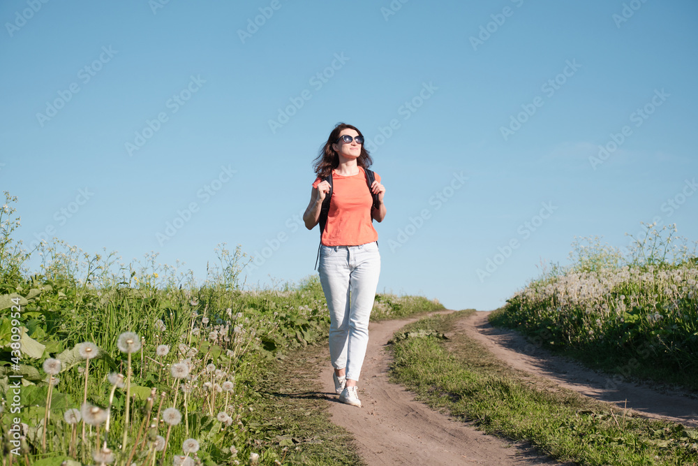 A girl with a backpack walks along a stone road. Around green plants and sunny w