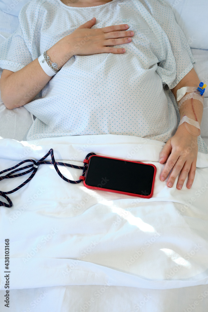 Pregnant woman on drip at hospital waiting a call from her smartphone Pregnant woman on drip at hospital waiting a call from her smartphone