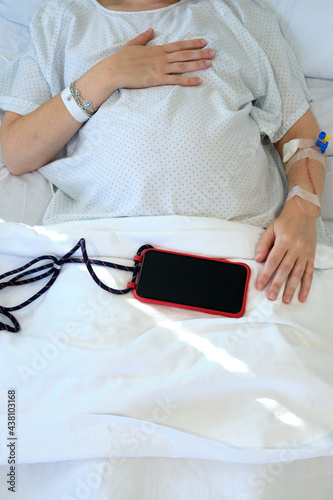 Pregnant woman on drip at hospital waiting a call from her smartphone