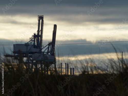 Two mighty cranes at Teesport Container Facility in near silhouette and dinosaur-like, against a luminous, cloud-striped winter sky. photo