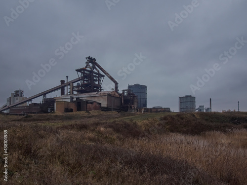 The derelict, abandoned hulk of the blast furnace at the Redcar Steelworks against a clouded sky, seen from the dunes of Coatham Marshes.