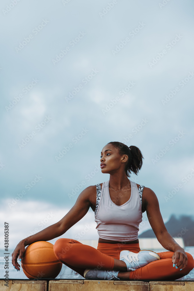 Fototapeta premium Sportswoman with basketball relaxing on rooftop