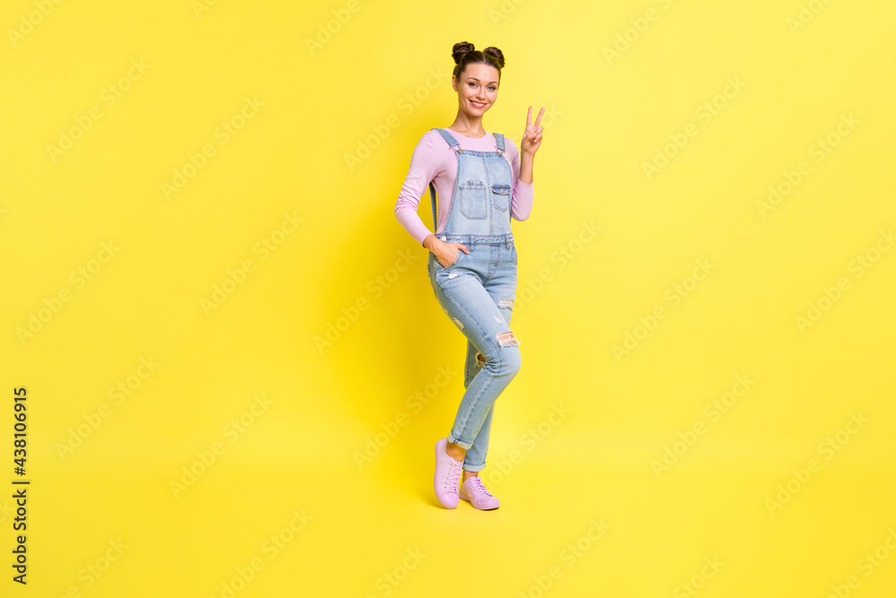 Photo of charming young girl posing show v-sign shiny toothy smile wear denim overall shoes isolated yellow background Photo of charming young girl posing show v-sign shiny toothy smile wear denim overall shoes isolated yellow background