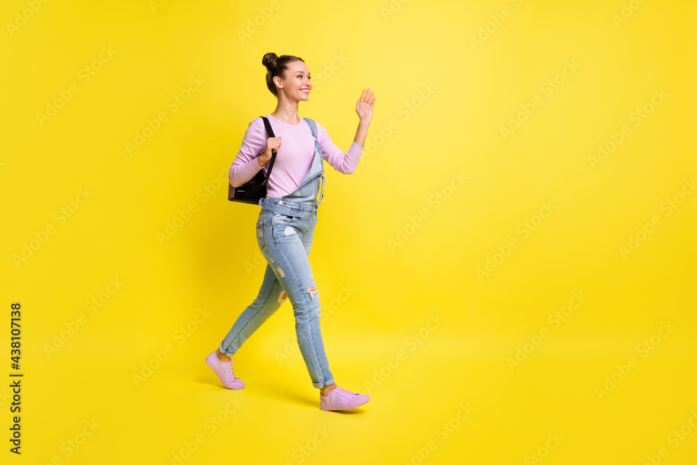 Full size profile photo of optimistic nice brunet lady go wave hand wear overall isolated on yellow background Full size profile photo of optimistic nice brunet lady go wave hand wear overall isolated on yellow background