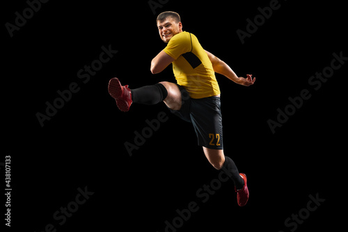 Powerful, flying above the field. Young football, soccer player in action, motion isolated on black background .