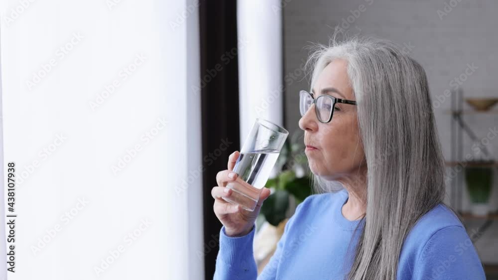 Smiling beautiful elderly gray-haired woman holding glass of water and drinking. Healthcare and wellbeing lifestyle. Drinking Water. Diet concept. Healthy Eating. Smiling beautiful elderly gray-haired woman holding glass of water and drinking. Healthcare and wellbeing lifestyle. Drinking Water. Diet concept. Healthy Eating.