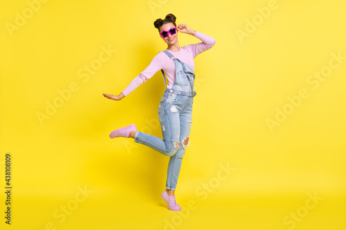 Photo of sweet cool young lady dressed jeans overall dark glasses dancing isolated yellow color background