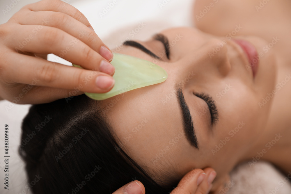 Young woman receiving facial massage with gua sha tool in beauty salon, closeup