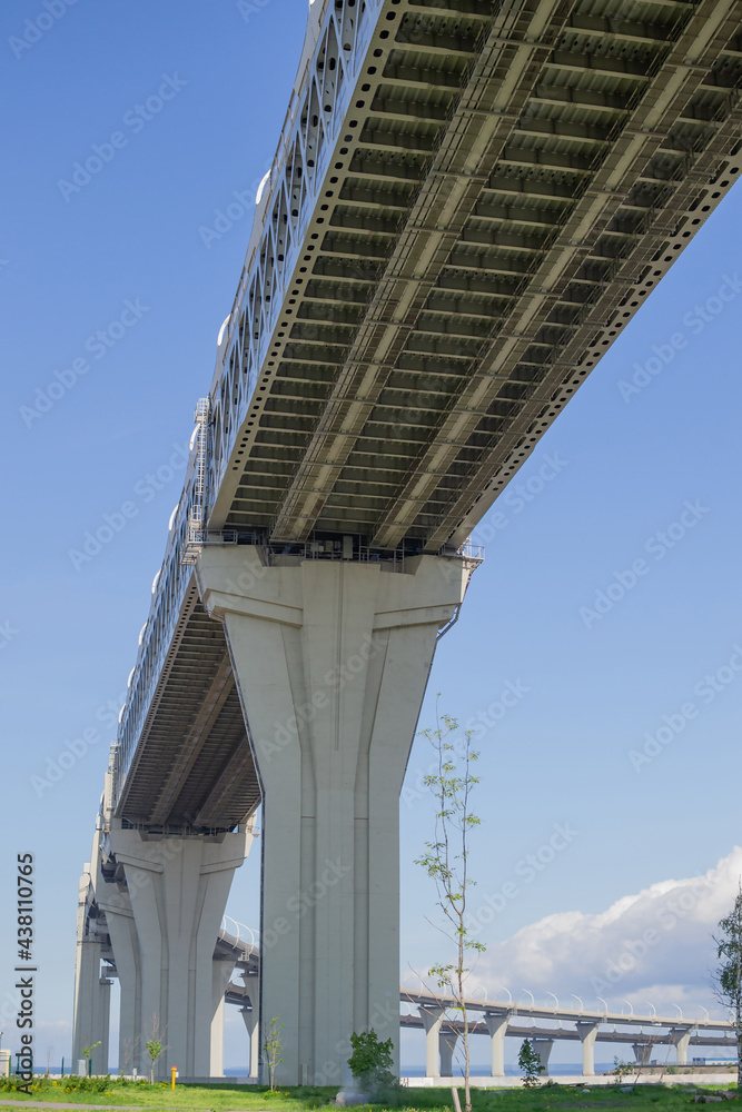 View of the rounded highway bridge from below against the blue sky. The road passing over the green embankment of the city, perspective. Controlled-access highway View of the rounded highway bridge from below against the blue sky. The road passing over the green embankment of the city, perspective. Controlled-access highway