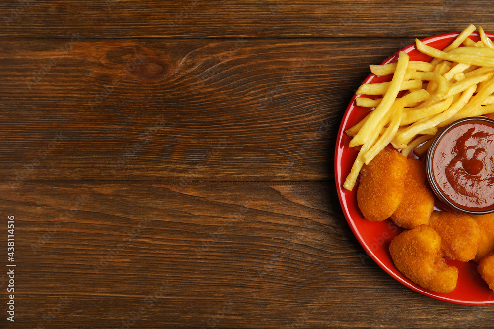 Tasty chicken nuggets and French fries served with ketchup on wooden table, top view. Space for text Tasty chicken nuggets and French fries served with ketchup on wooden table, top view. Space for text