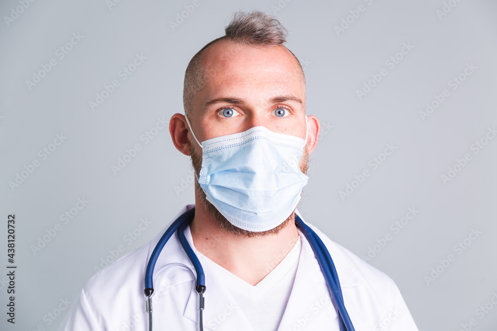 Handsome male doctor on gray background with protective medical mask on face Handsome male doctor on gray background with protective medical mask on face