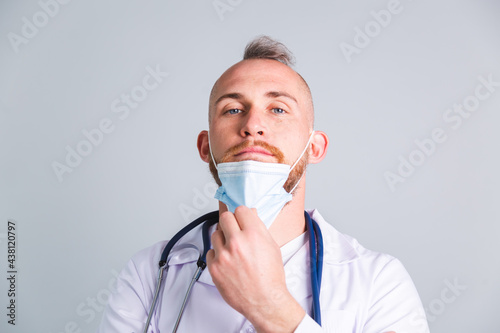 Handsome male doctor on gray background with takes off protective medical mask