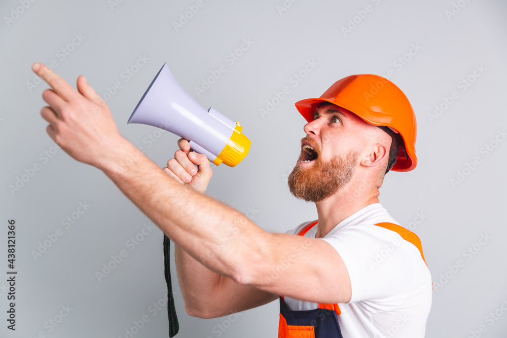 Handsome man engineer in building protective helmet on gray background shouting screaming in megaphone Handsome man engineer in building protective helmet on gray background shouting screaming in megaphone