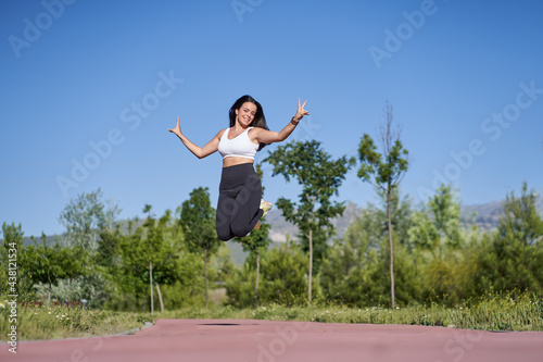 Young woman with fit body jumping. Female model in sportswear exercising and headphones