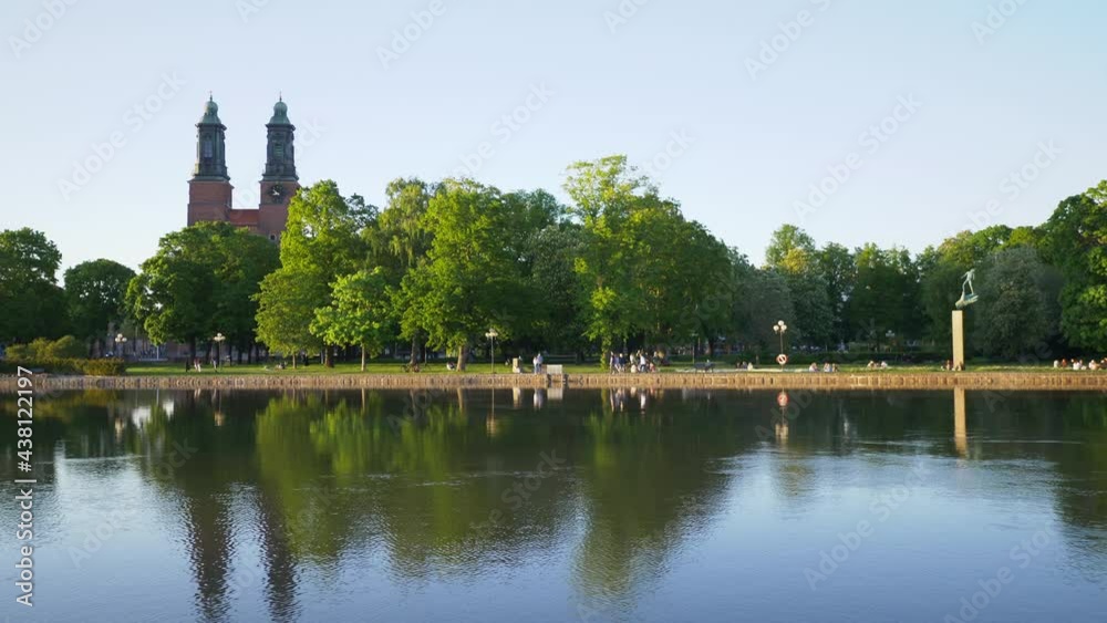 Eskilstuna, Sweden - May 30, 2021. People relaxing with sunny in summer and midsummer festival on river side public park near Klosters kyrka church landmark building