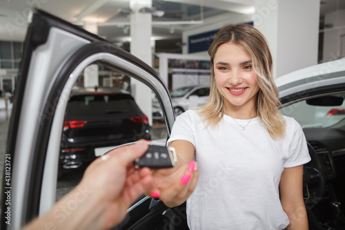 Beautiful happy woman receiving car keys to her new automobile at car dealership