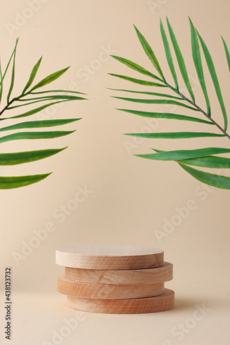 Cosmetic background with wooden podium and palm leaves on pastel beige. Empty showcase for cosmetic product presentation.