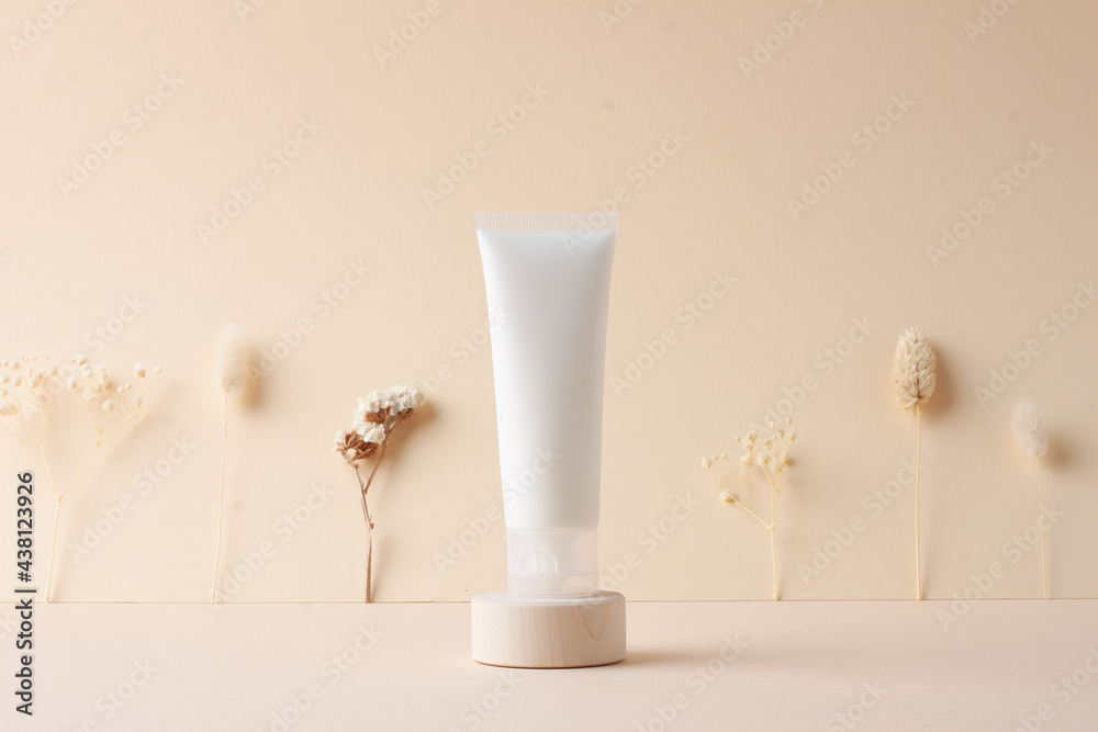 White tube of cosmetic cream with flowers on wooden podium on beige background. Close up. White tube of cosmetic cream with flowers on wooden podium on beige background. Close up.